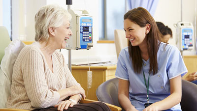 Picture of a female Nurse sitting next to an elderly female patient. They are both laughing and smiling.