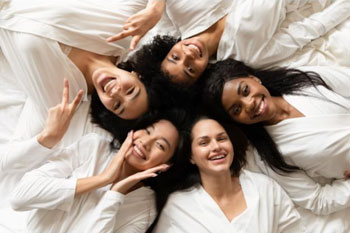 Picture of five smiling females laying down, next to one another with their heads each touching.